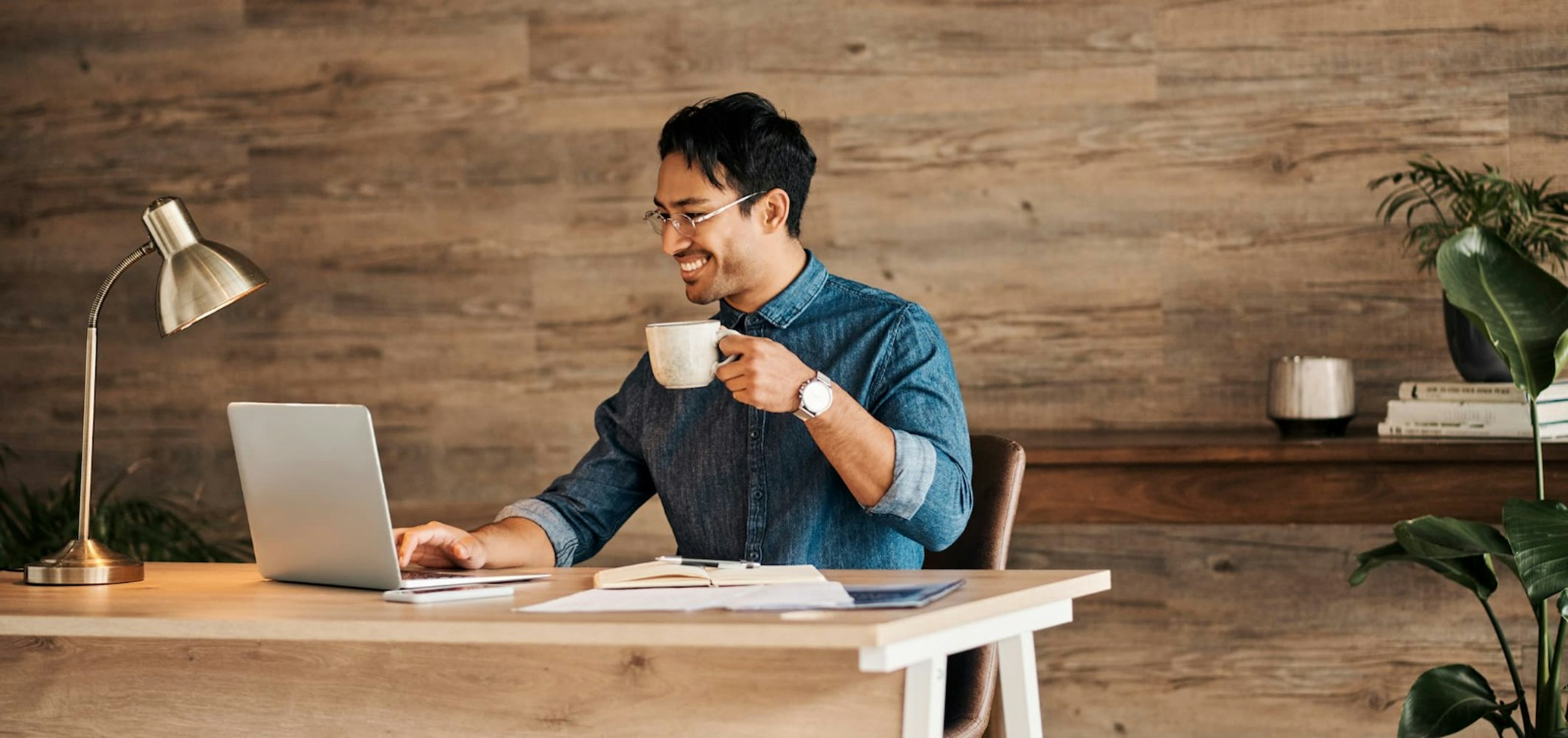Man at desk drinking coffee and working on his laptop